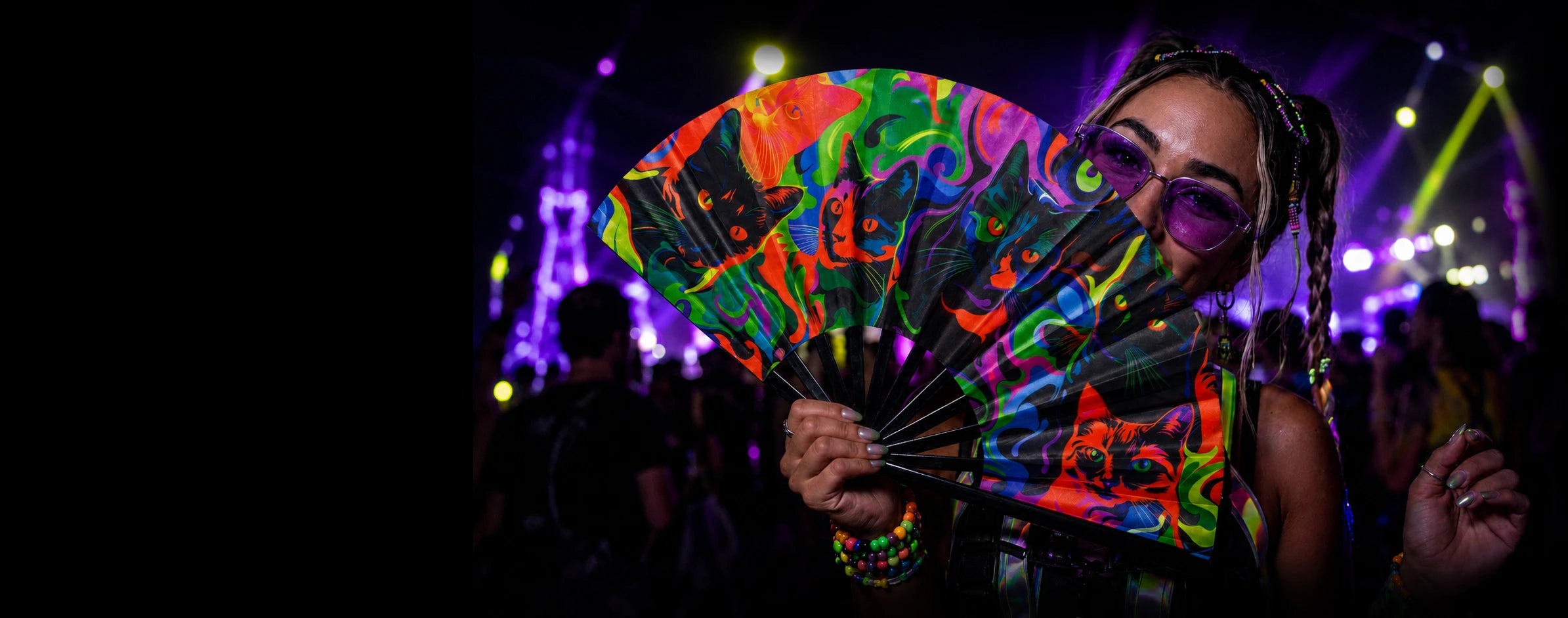 Raver holding Funxtuff UV-reactive folding fan with wrist strap, neon cat print, at outdoor music festival